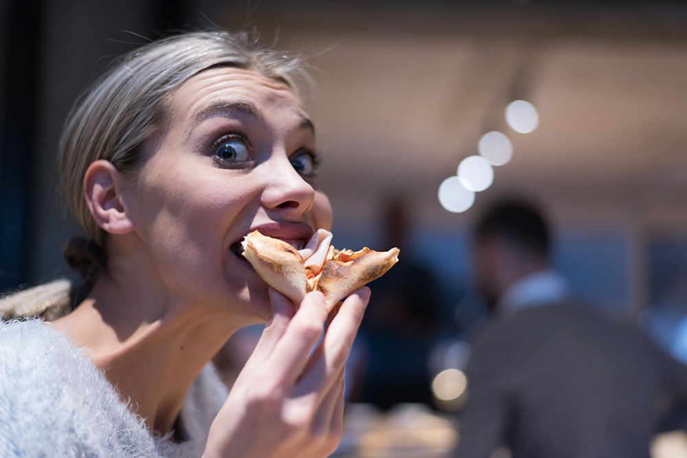 woman eating a slice of pizza with a silly face