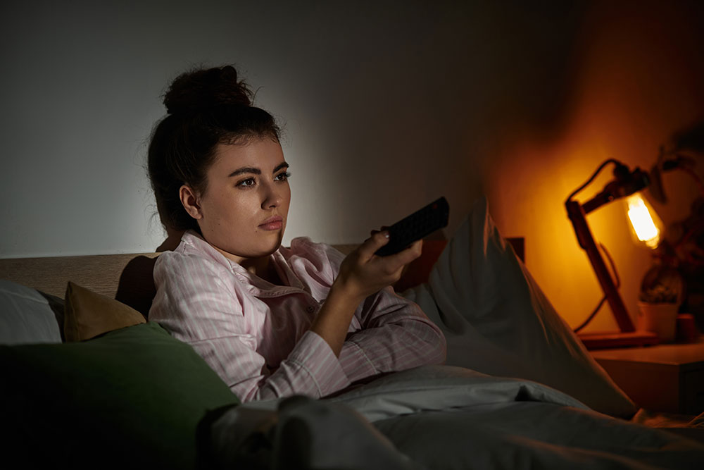 woman in bed at night holding a remote and watching tv